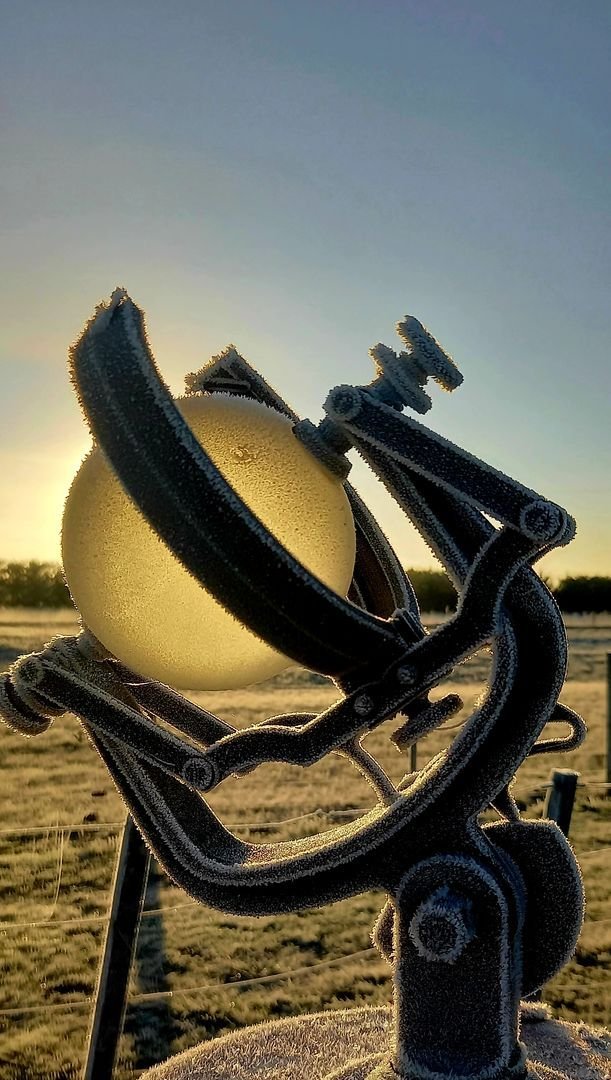 Heliofanógrafo con escarcha sobre su pedestal, con el sol de la mañana detrás de la esfera.